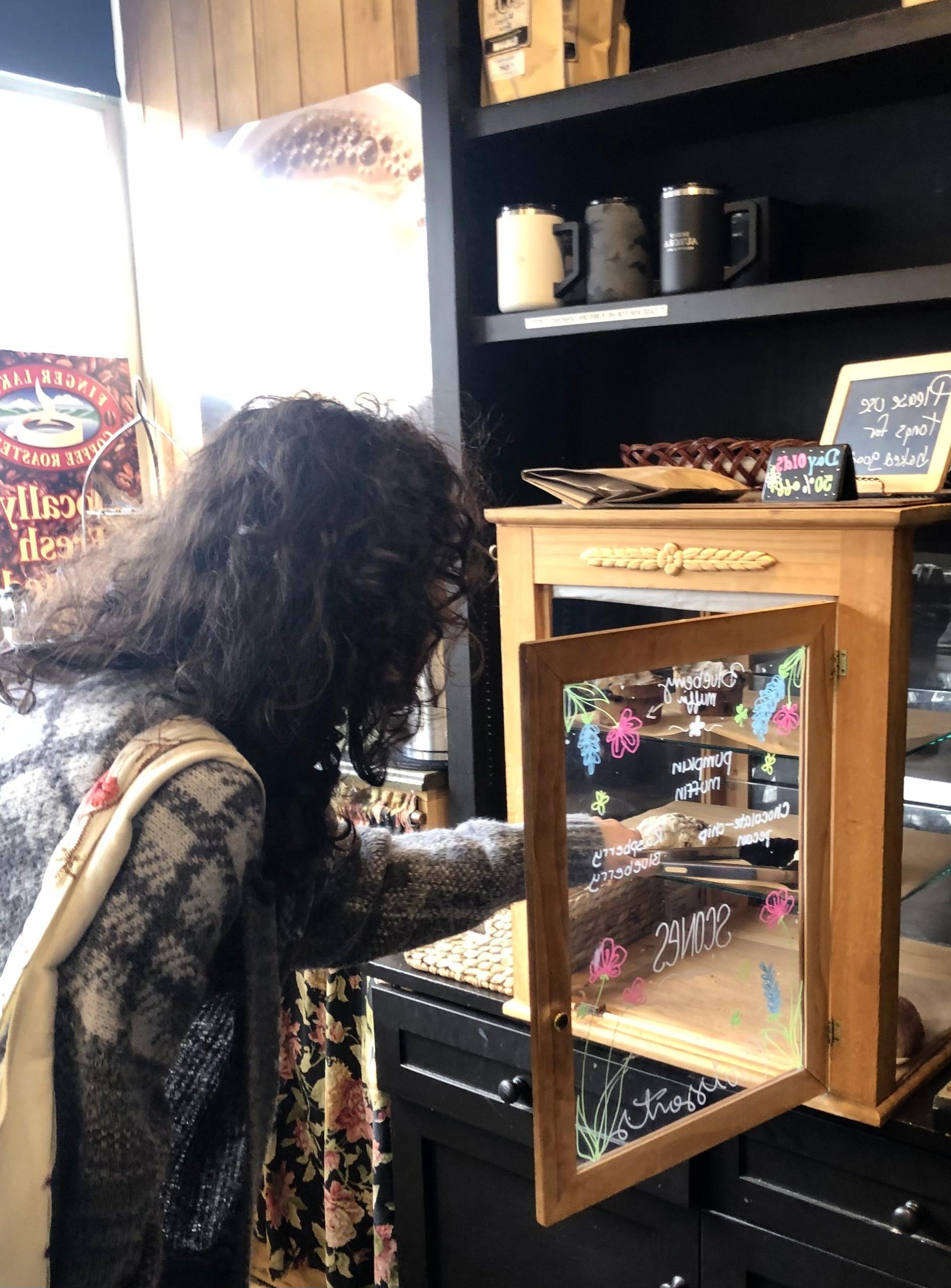 woman with dark hair helping herself to a sweet treat from a glass case